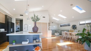A modern kitchen with a central island, wooden flooring, and a dining area with white furniture.