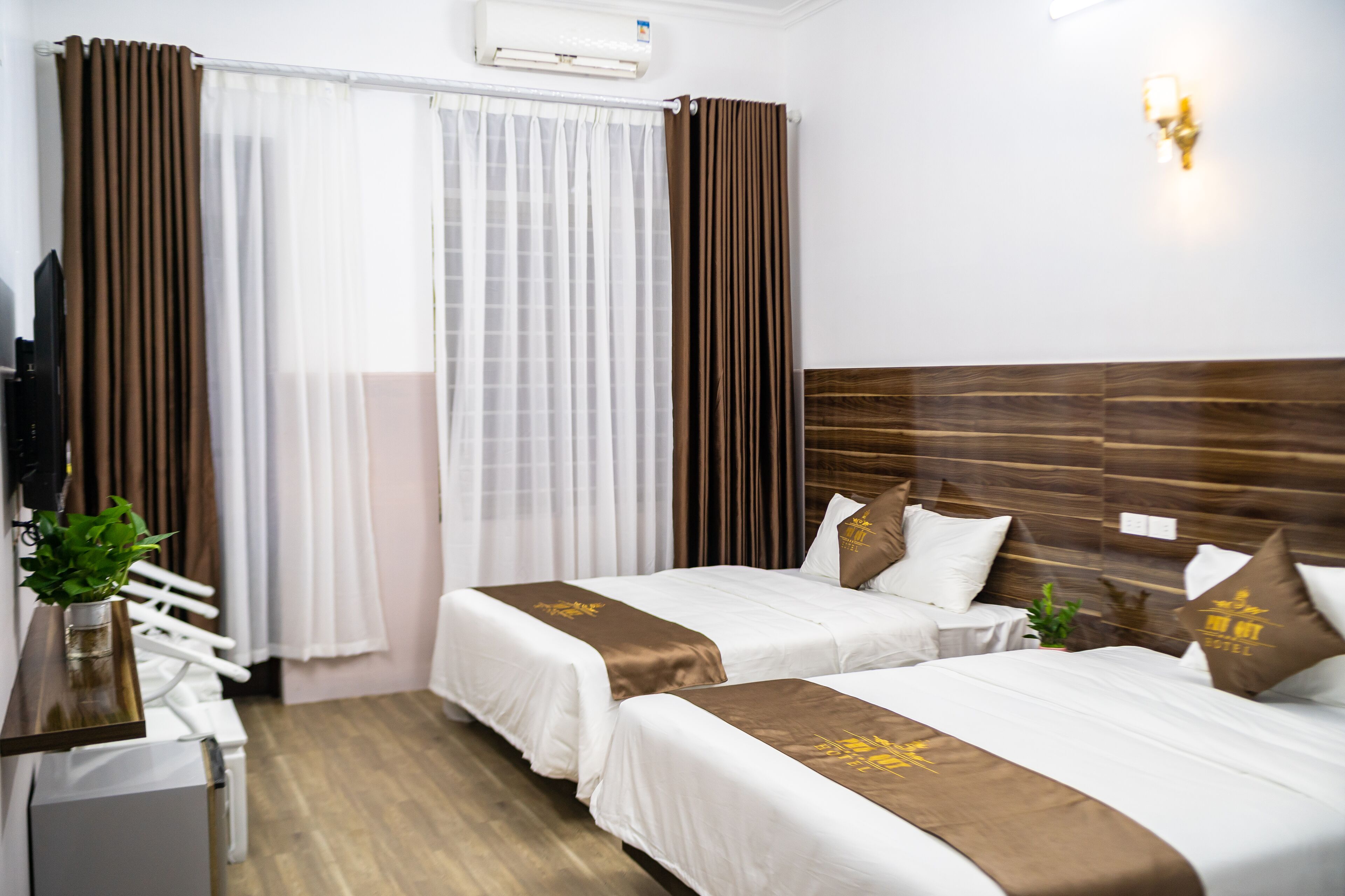 Habitación de hotel con dos camas, televisión, escritorio y una planta.