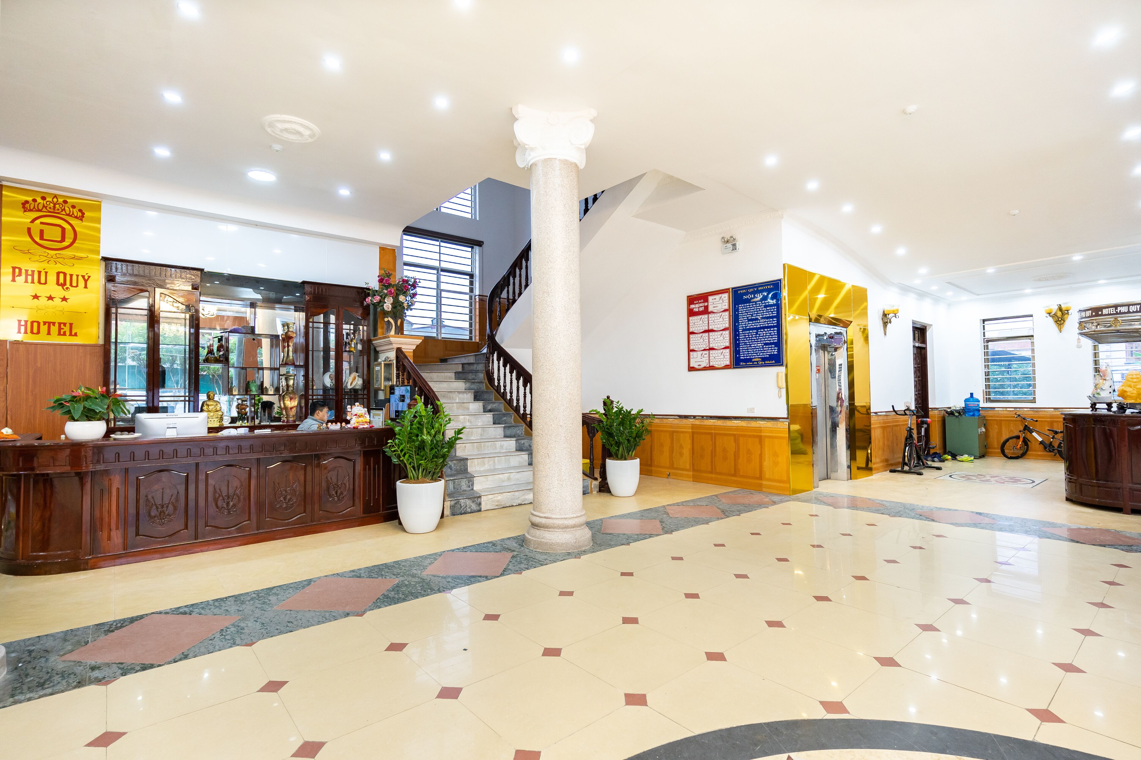 Um hall de hotel com uma mesa de recepção, escada e um grande pilar.