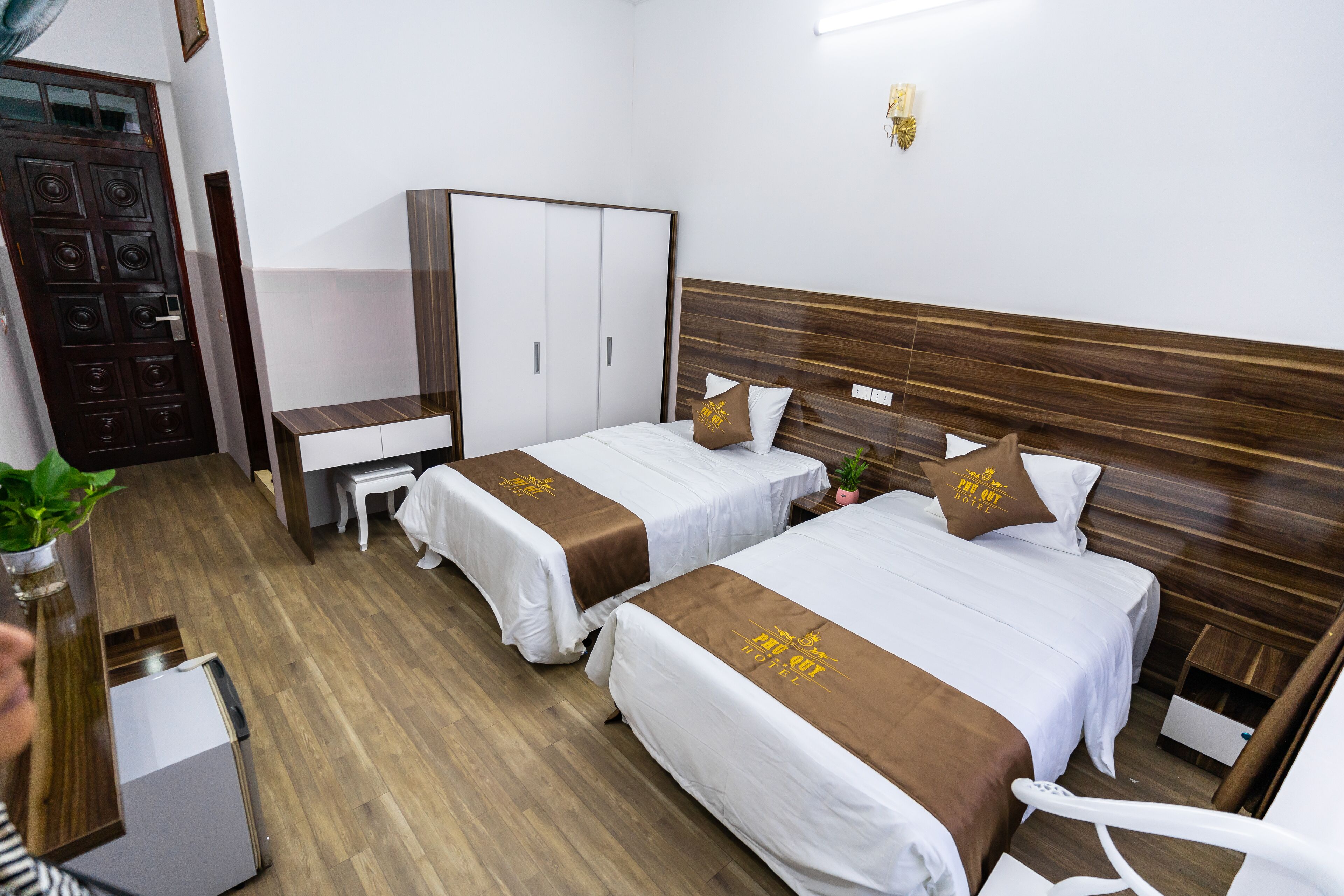 A hotel room with two beds, a wardrobe, a desk, and a small table.