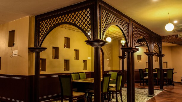 Un comedor con una mesa alta, sillas, columnas de madera y suelo estampado.