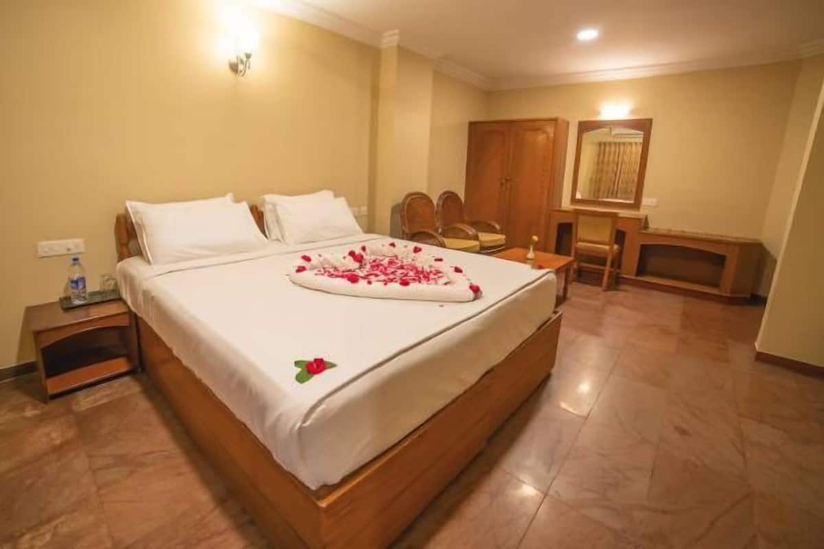Habitación de hotel con una cama grande, una mesita de noche de madera, una silla, una pequeña mesa y un espejo.
