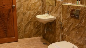 Un baño con pared de mármol, puerta de madera, lavamanos, inodoro y una toalla en el suelo.