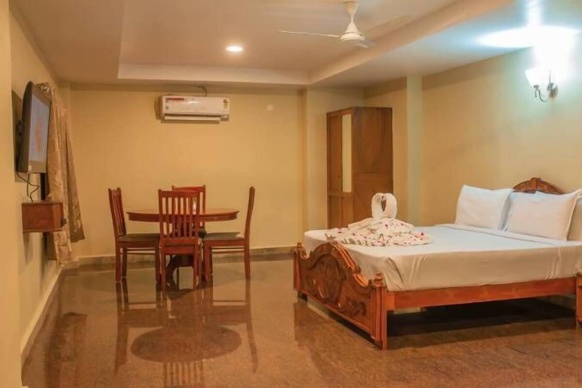 Una habitación de hotel con una cama de madera, una mesita con sillas, un aire acondicionado y un ventilador de techo.