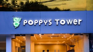Entrada de un hotel con un letrero que dice "POPPYS TOWER" y un logo verde.