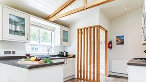 A modern kitchen with white cabinetry, a wooden beam ceiling, and a view to the outside. - Netherfield Watersedge Lodge (Newton Saint Loe, Nr Bath)