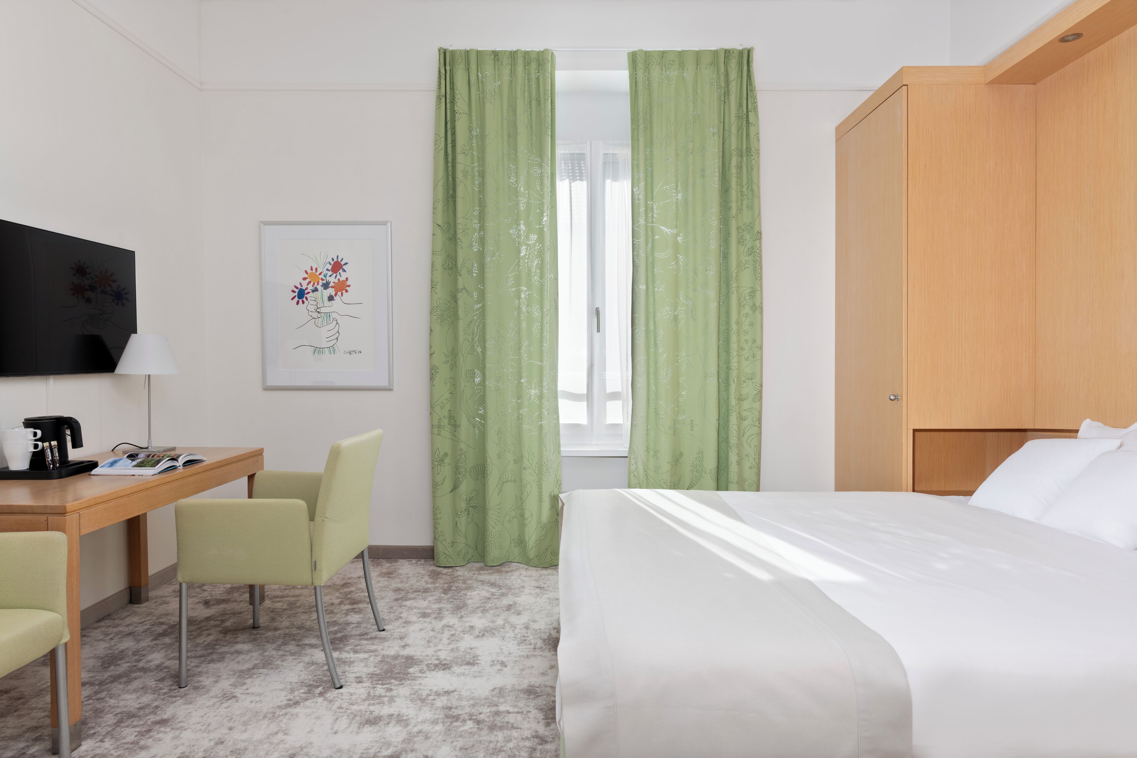 A hotel room with a bed, a desk with a chair, a television, and green curtains.