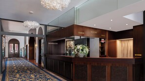 A reception area with a wooden counter, a blue carpet, and a chandelier. - Grand Hotel Europe (Lucerne)