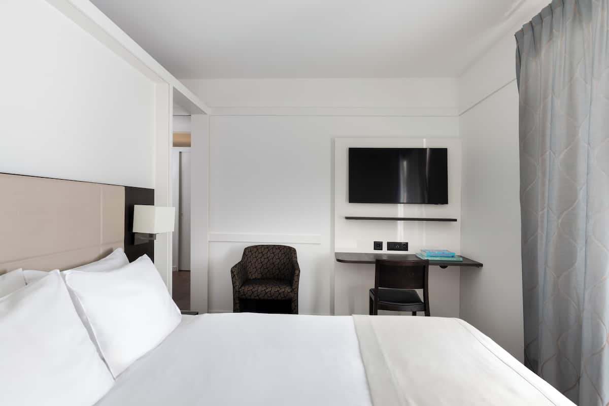 Ein Hotelzimmer mit einem Bett, einem Schreibtisch mit Fernseher, einem Sessel und einer Lampe.