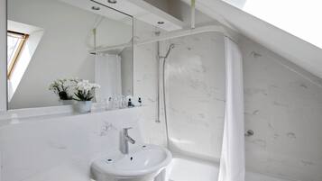 A modern bathroom with a white sink, a shower, and a large mirror.