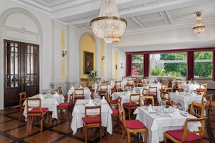 Un comedor formal con varias mesas dispuestas para el servicio, sillas de madera con cojines rojos y un candelabro.