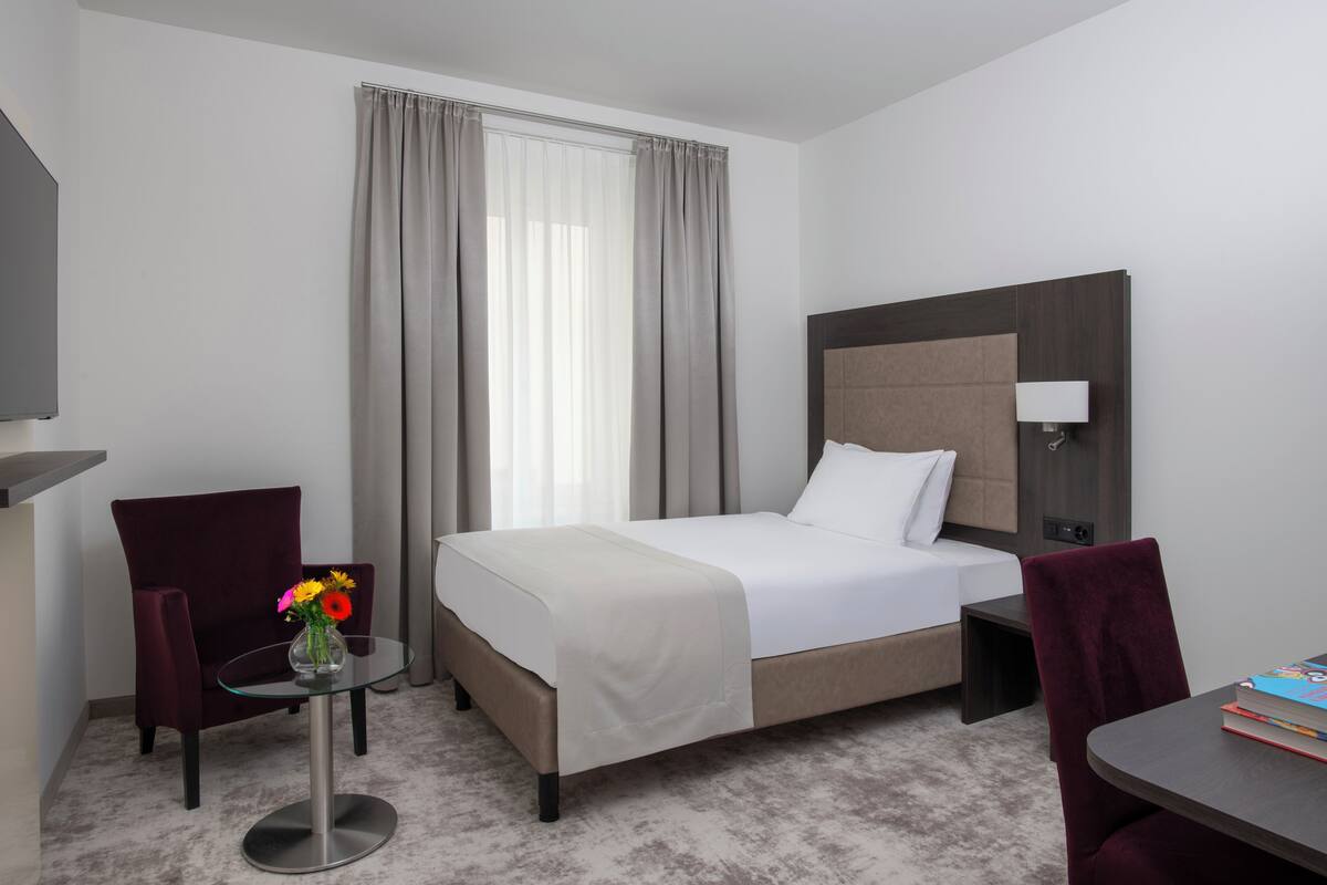Ein Hotelzimmer mit Bett, Schreibtisch, Stuhl und einem kleinen Tisch mit Blumen.