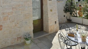 Un edificio de piedra con una entrada pequeña, una mesa con sillas y una planta en maceta.