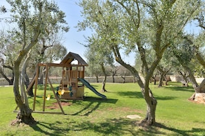 Explore a serene play area surrounded by lush greenery and a wooden playhouse with a slide.