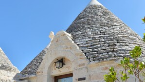 A stone building with a conical roof, a door with a glass panel, and a table with chairs outside.