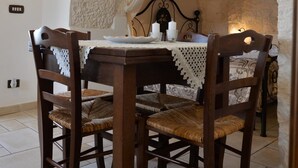 A dining area with a stone arch, a table with a lace tablecloth, wooden chairs, and an air conditioning unit above.