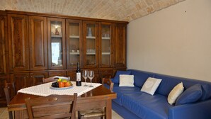 Uma área de refeições com mesa de madeira, cadeiras, um sofá azul e um armário com portas de vidro.