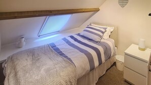 A bedroom with a bed, a bedside table, a nightstand, a window, and a wall decoration. - 2 bedroom accommodation in Pontyberem, Carmarthenshire (Pontyberem, Carmarthenshire)