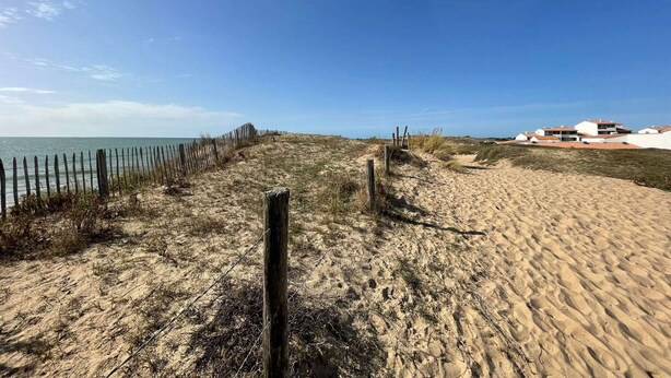 A sandy beach path leading to a building with multiple floors and flat roofs. - 1-Bedroom Apartment near Beach, Saint-Hilaire-de-Riez (Saint-Hilaire-de-Riez)