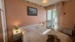 A bedroom with a large bed, two bedside tables with lamps, a window with curtains, and a radiator. - 1-Bedroom Apartment near Beach, Saint-Hilaire-de-Riez (Saint-Hilaire-de-Riez)