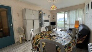 A compact living space with a dining table, chairs, a sofa, a TV, and a kitchenette. - 1-Bedroom Apartment near Beach, Saint-Hilaire-de-Riez (Saint-Hilaire-de-Riez)