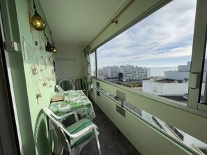A balcony with a table and chairs, a view of buildings, and a clear sky.