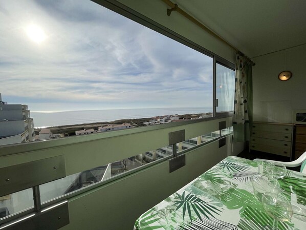 A room with a balcony overlooking a coastal area, a bed with a tropical leaf pattern, and a small table with glasses.