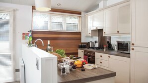 A modern kitchen with a central island, wooden accents, white cabinetry, and a built-in oven. - Carisbrooke Premier Lodge (Wootton, Nr Cowes)