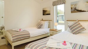A hotel room with two beds, a window with a view, a painting on the wall, and a lamp on the nightstand. - Carisbrooke Premier Lodge (Wootton, Nr Cowes)