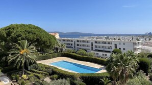 Un hotel con piscina rodeada de vegetación, vista al mar y un puerto deportivo al fondo.
