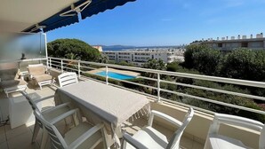 Un balcón con mesa y sillas, una piscina al fondo y vistas a un paisaje urbano.