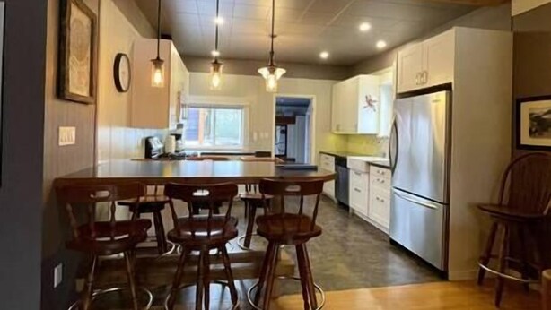 A kitchen with a central island, bar stools, a refrigerator, and pendant lighting. - Cozy, Warm & Spacious Fernie Bungalow (Fernie)