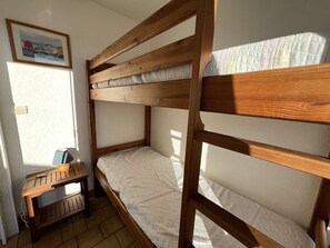 Quarto com beliche, uma escrivaninha pequena e um quadro na parede.