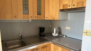 A compact kitchen with wooden cabinets, a stainless steel sink, a coffee maker, and a built-in oven. - Quiet Studio Cabin, Close to Beach, Washing Machine, Pets OK (Cap d'Agde)
