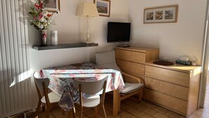 A small, well-lit room with a dining table, chairs, a TV, and a wooden cabinet. - Quiet Studio Cabin, Close to Beach, Washing Machine, Pets OK (Cap d'Agde)
