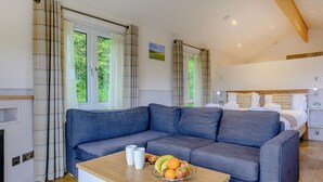Una habitación moderna con un sofá gris, una mesa de madera con fruta y una cama con ropa blanca.