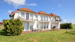 Une maison à deux étages, avec un toit recouvert de tuiles rouges, de grandes fenêtres et un balcon à l’étage supérieur.
