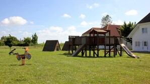 Un terrain de jeux avec une structure en bois, un toboggan et une petite voiture jouet orange.