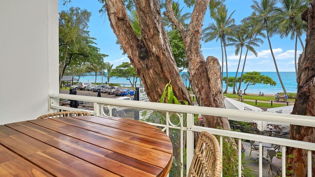 Ein Holztisch mit Stühlen auf einem Balkon mit Blick auf den Strand und Palmen.
