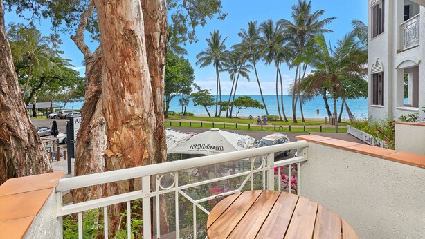A balcony with a view of the ocean, palm trees, and a building labeled "CAFE BAR".