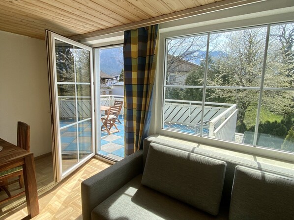 Une pièce comprenant un canapé, une table à manger et donnant sur un balcon aménagé avec du mobilier d’extérieur.