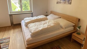 A bedroom with a wooden bed, a window with a view of greenery, and a radiator below the window. - salzkammergut lake region (ebensee) - 8 pers. - pets welcome - garden - terrace (Ebensee)