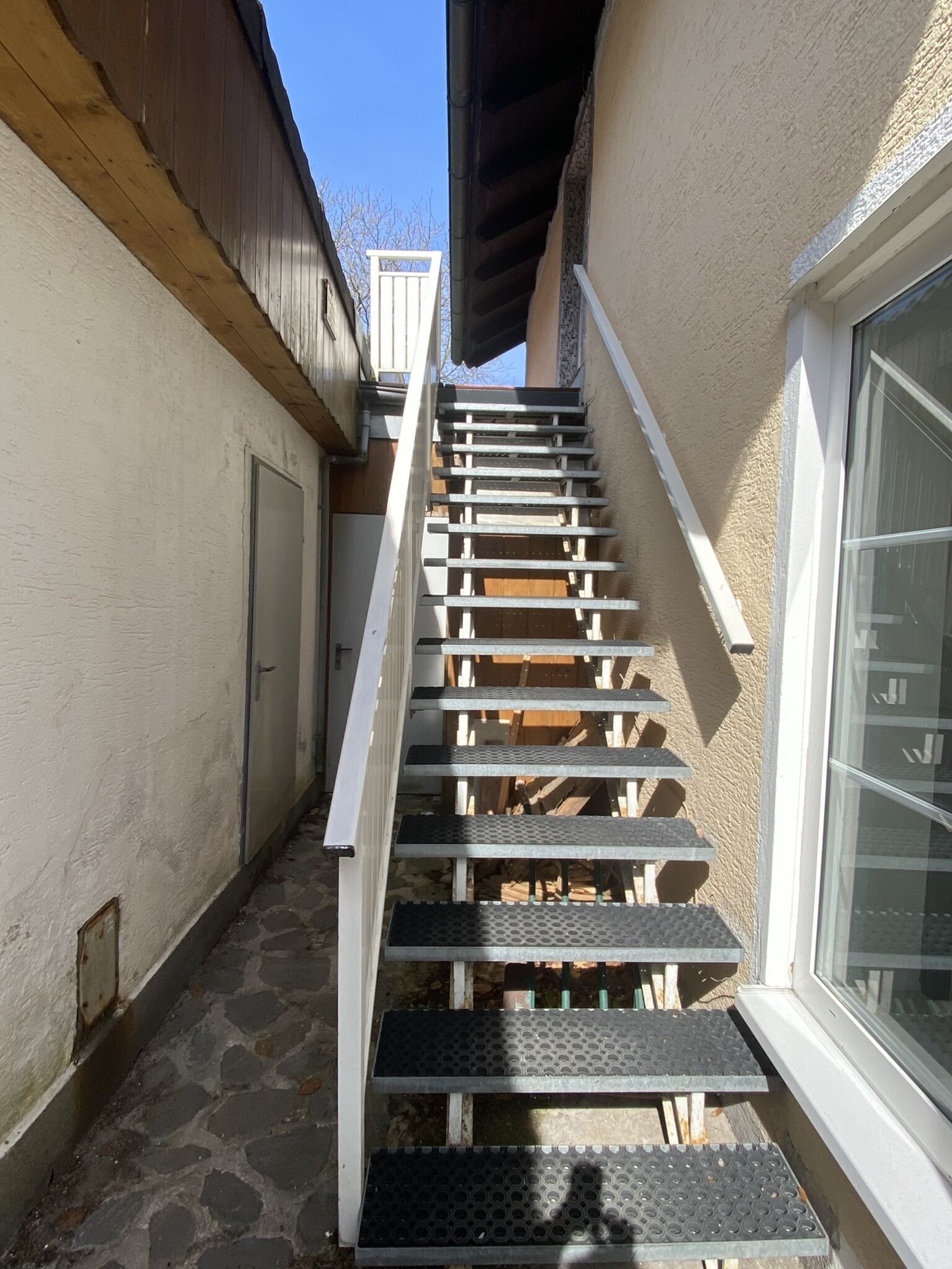 A narrow outdoor staircase with metal steps and wooden handrails, leading to a door at the top.