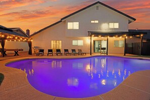 Une maison avec une piscine, un espace salon extérieur et des guirlandes lumineuses.