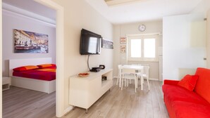 A modern living room with a bed, a TV, a dining table, and a red sofa. - A Pass by St. Peter's 121 (Roma)
