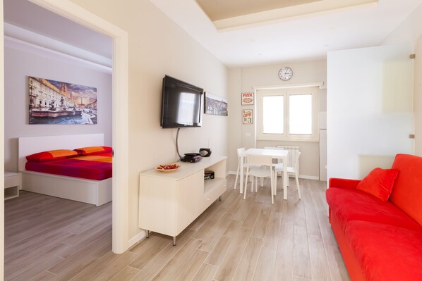 Uma sala de estar moderna com uma cama, uma TV, uma mesa de jantar e um sofá vermelho.