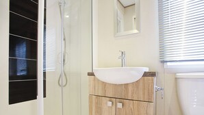 A bathroom with a glass shower enclosure, a wooden vanity with a sink, and a toilet. - 2 bedroom accommodation in Newquay (Newquay)