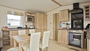 A compact kitchen with a microwave, toaster, stove, and wooden cabinets. - 2 bedroom accommodation in Newquay (Newquay)