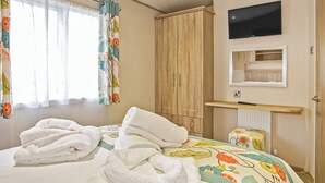 A bedroom with a bed, towels, a wardrobe, a television, and a mirror. - 2 bedroom accommodation in Newquay (Newquay)