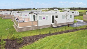 A row of mobile homes with a grassy lawn, a paved driveway, and a clear sky. - 2 bedroom accommodation in Newquay (Newquay)